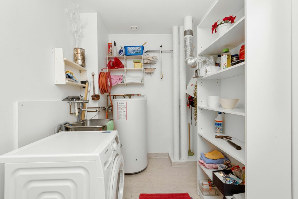 Clean and organized home laundry room with washing machine, shelves, and water heater.