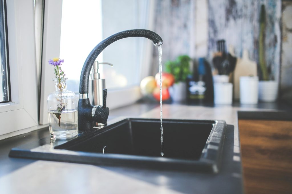 A modern kitchen sink with running water, a sleek faucet, and a vase on the countertop.